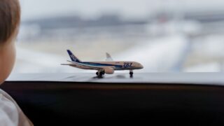 空港の窓際でANAの飛行機ミニチュアを眺める子供