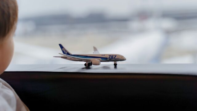 空港の窓際でANAの飛行機ミニチュアを眺める子供