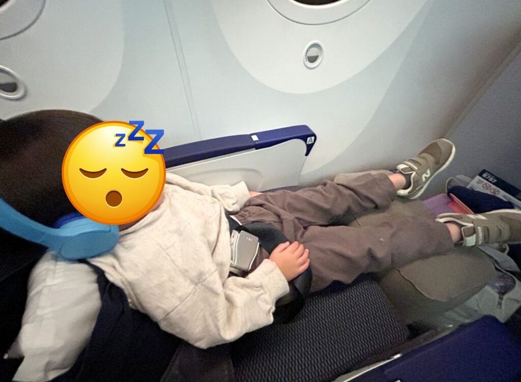 飛行機の座席でフットレストに足を乗せ、体を伸ばして眠る子ども