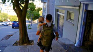 コロンビアのバックパックを背負い、子どもを抱っこして海外の街を歩く後ろ姿