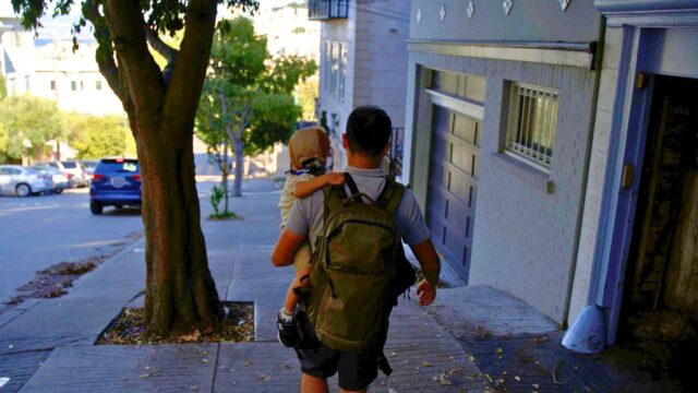 コロンビアのバックパックを背負い、子どもを抱っこして海外の街を歩く後ろ姿