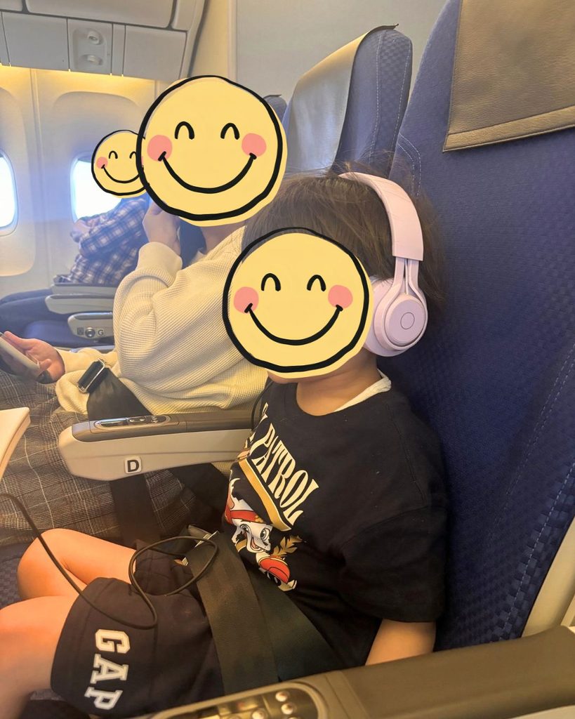 飛行機の座席で、子ども用ヘッドホンを有線でつないで機内モニターを見る子ども